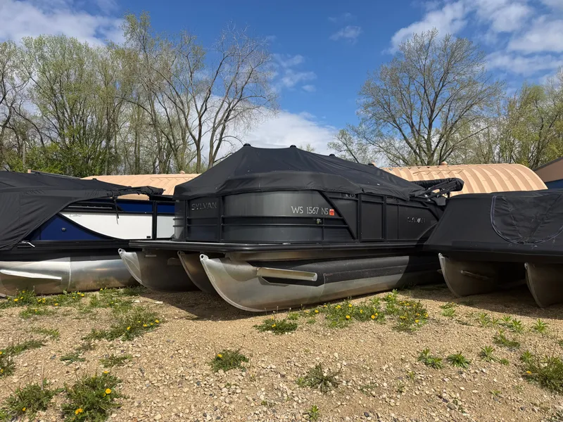 The Image of 2023 Sylvan L-3 PF TT pontoon boat with cover on gravel surface. - 0