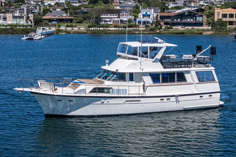 The Image of 1979 Hatteras 58 Motor Yacht cruising on a serene blue lake near waterfront homes. - 1