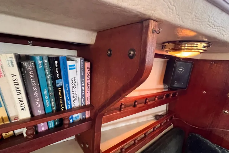 Slide: The Image of Bookshelf inside a 1984 Catalina 30 sailboat with nautical-themed books and a speaker. - 37