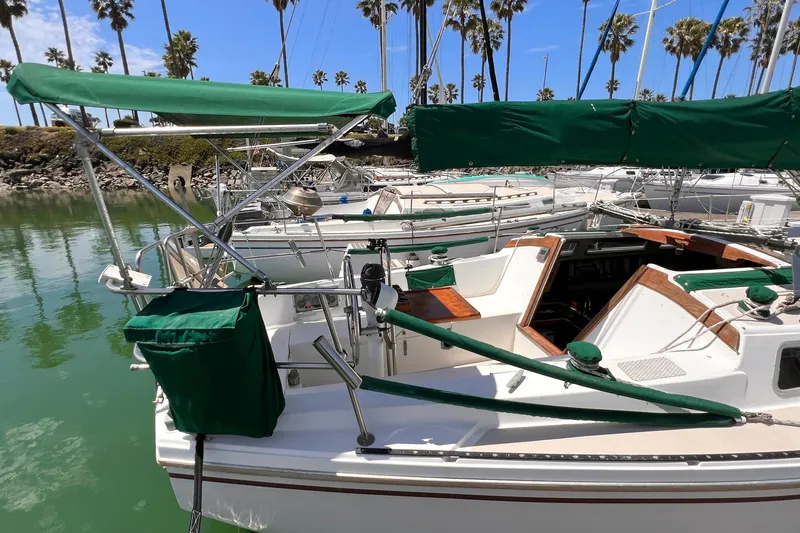 Slide: The Image of 1984 Catalina 30 sailboat docked, featuring green canvas covers and a scenic marina backdrop. - 6