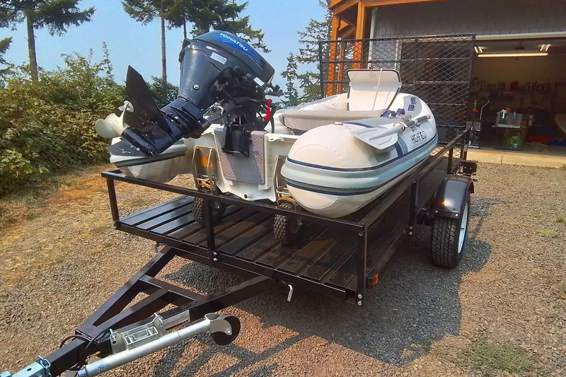 Slide: The Image of Trailer with inflatable boat and outboard motor, parked outdoors near a garage. - 25