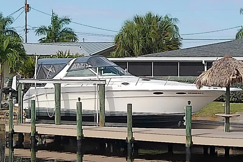 The Image of 1998 Sea Ray Sundancer 330 docked near a waterfront home with tropical landscaping. - 0