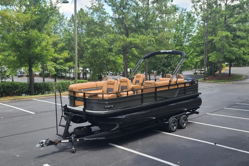 Slide: The Image of 2026 Ranger 223FC pontoon boat with tan seating, parked in a tree-lined lot. - 4
