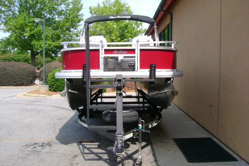Slide: The Image of 2026 Sun Tracker Bass Buggy 18 DLX pontoon boat on trailer, parked outdoors. - 6