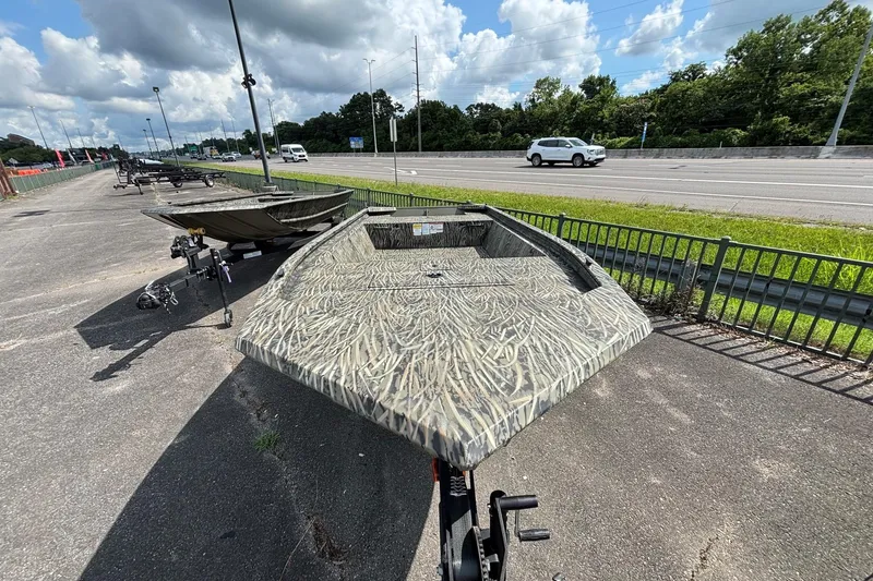 Slide: The Image of 2026 Tracker Grizzly 1648 Utility boat with camouflage design parked near a highway. - 2