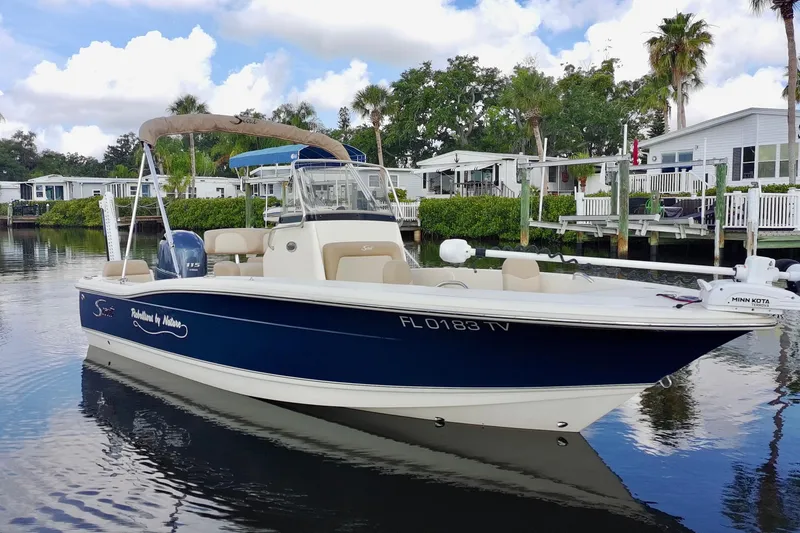 Slide: The Image of 2024 Scout 195 Sportfish boat on calm water, surrounded by waterfront homes. - 11