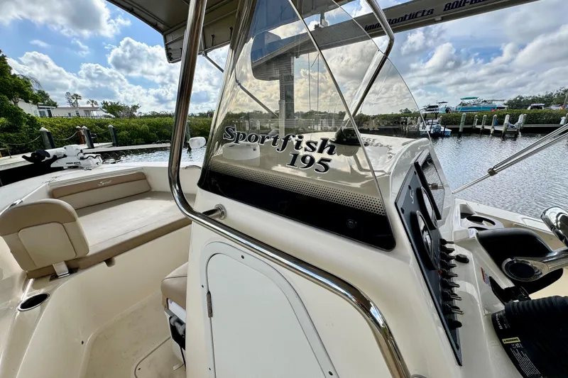 Slide: The Image of 2024 Scout 195 Sportfish boat interior with console and seating, docked by a scenic waterfront. - 31