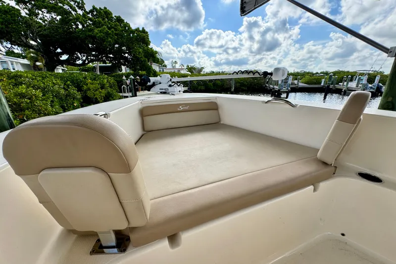 Slide: The Image of 2024 Scout 195 Sportfish boat interior with beige seating, docked by lush greenery. - 35