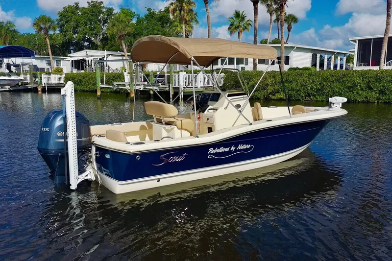 Slide: The Image of 2024 Scout 195 Sportfish boat with canopy on calm water, surrounded by lush greenery. - 9