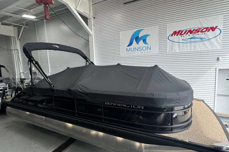 Slide: The Image of 2024 Bennington 24 L Swingback pontoon boat with cover in showroom, Munson Ski & Marine signs visible. - 27