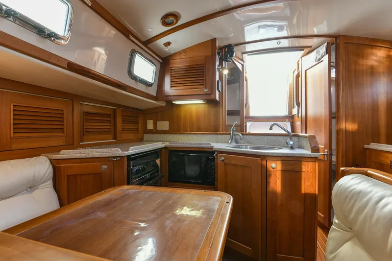Slide: The Image of Interior of a 1999 Gozzard 37A yacht featuring a wooden kitchen and dining area. - 24