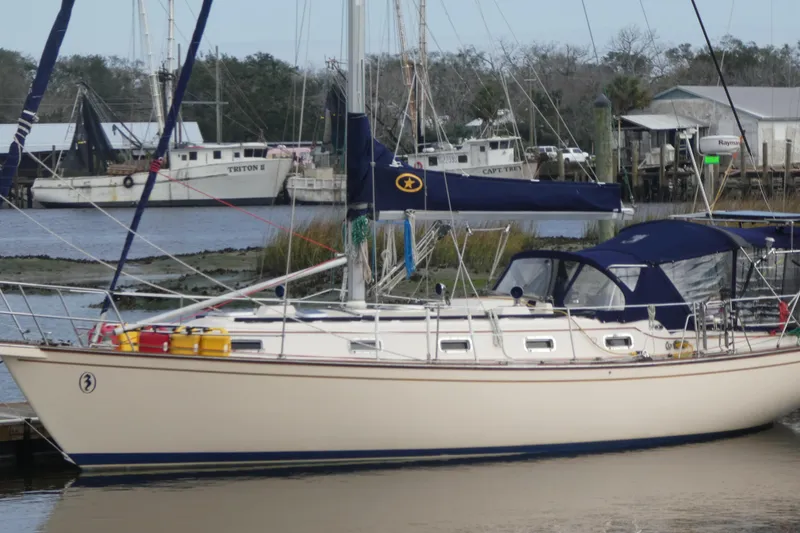 Slide: The Image of 1995 Island Packet 37 sailboat docked at a marina, featuring a beige hull and blue canopy. - 83