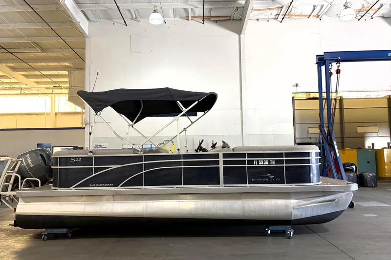 The Image of 2023 Bennington S22 pontoon boat in a warehouse, featuring a black canopy. - 1