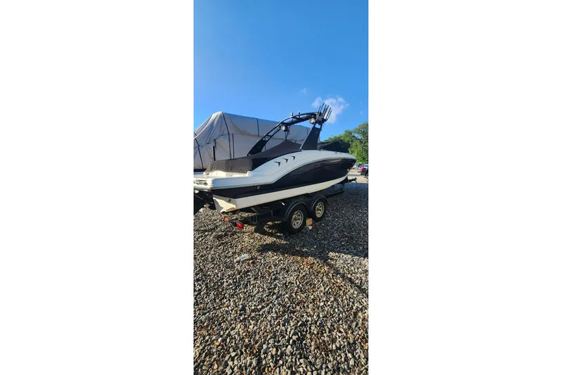 Slide: The Image of 2019 Chaparral 23 H2O Sport boat on trailer, parked on gravel under clear blue sky. - 14