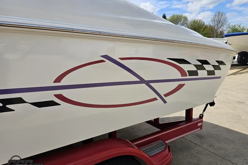 Slide: The Image of 1999 Baja 272 boat with colorful graphics on a red trailer, parked outdoors. - 26