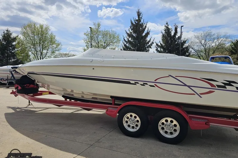 Slide: The Image of 1999 Baja 272 speedboat on red trailer, parked outdoors under cloudy sky. - 28