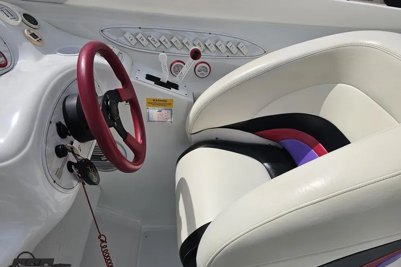 Slide: The Image of Interior of a 1999 Baja 272 boat featuring a red steering wheel and white seating. - 56