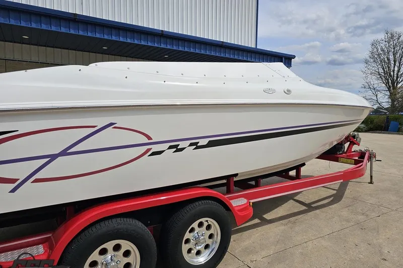 Slide: The Image of 1999 Baja 272 boat on red trailer, parked outdoors near a building. - 8