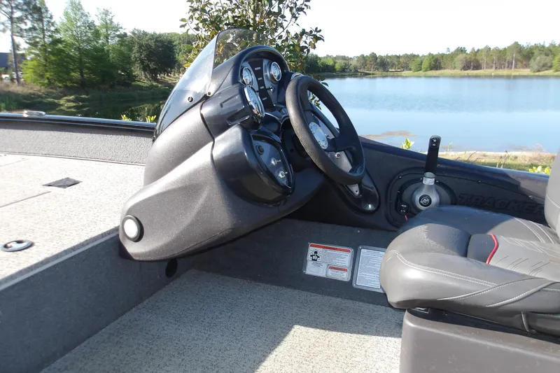 Slide: The Image of 2023 Tracker Pro Team 175 TXW boat interior with steering wheel and dashboard by a lake. - 6