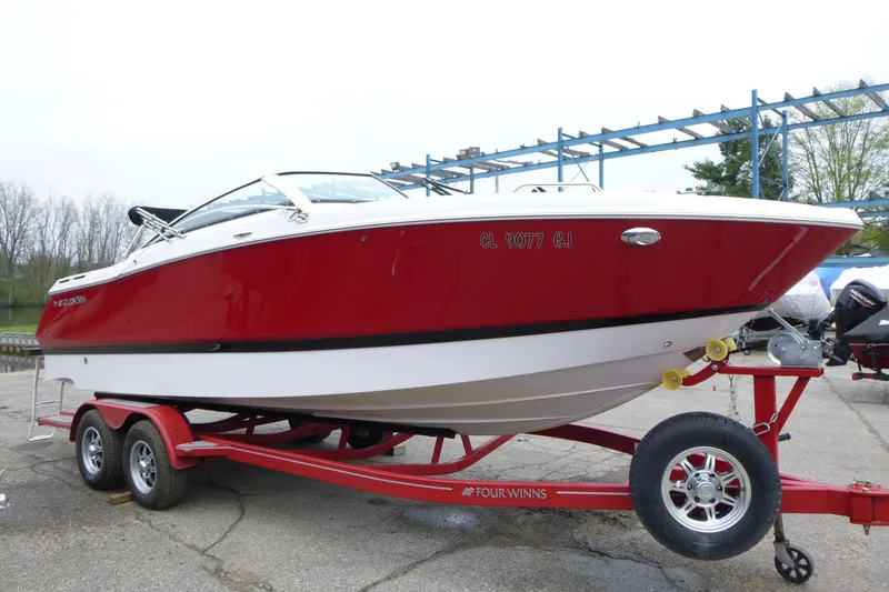 The Image of 2017 Four Winns H260 boat in red and white on a trailer, parked outdoors. - 1