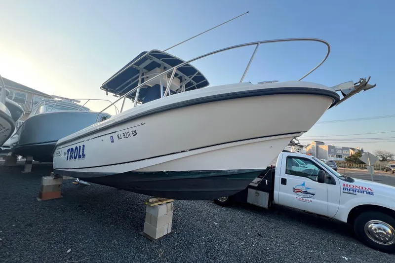 Slide: The Image of 1998 Boston Whaler Outrage 23 boat on display, elevated on blocks, near a Honda Marine truck. - 4