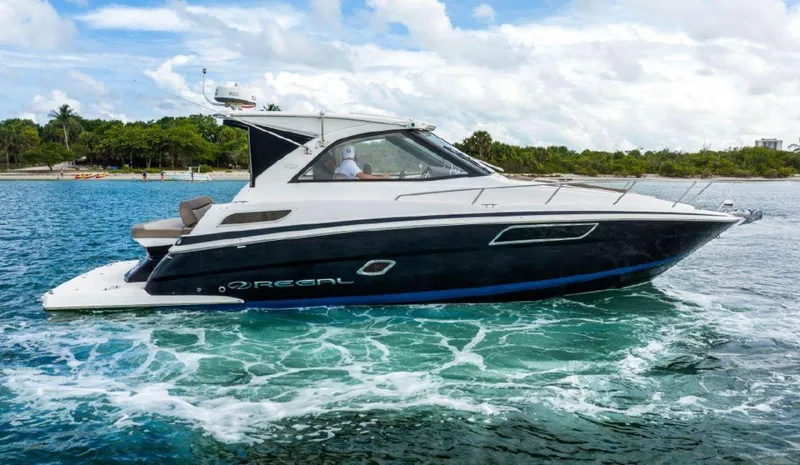 The Image of 2015 Regal 35 Sport Coupe cruising on blue water near a lush shoreline. - 0