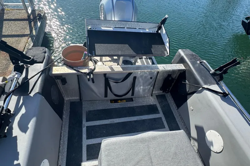 Slide: The Image of 2022 Bullfrog 17ft Pilot House boat interior with fishing gear and motor, docked on water. - 7