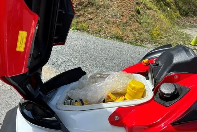 Slide: The Image of 2012 Kawasaki Jetski Ultra LX storage compartment with items, parked on gravel road. - 11