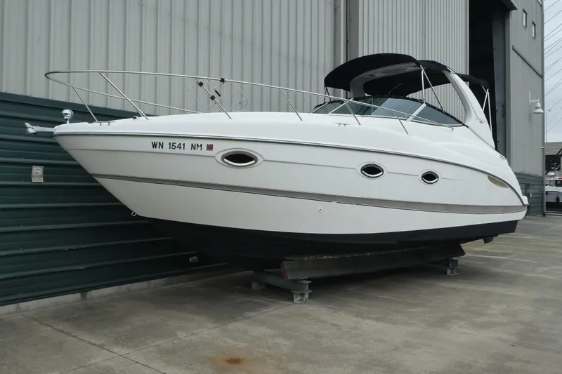 The Image of 2002 Maxum 3100 SCR boat on dry dock, white hull, near industrial building. - 0
