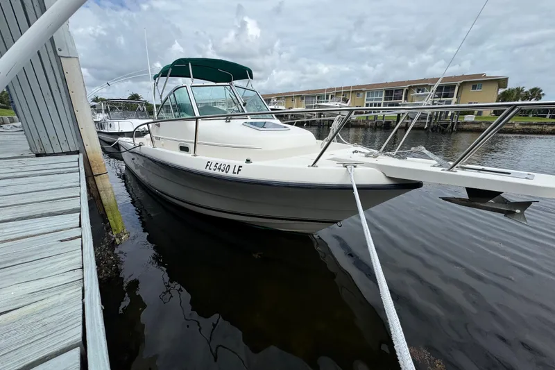 The Image of 2000 Pursuit 2470 Walkaround boat docked at marina, featuring green canopy and white hull. - 0