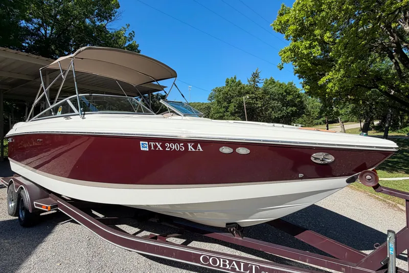 Slide: The Image of 2004 Cobalt 250 boat on trailer, maroon and white, parked outdoors under clear sky. - 6