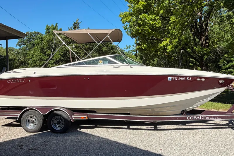 Slide: The Image of 2004 Cobalt 250 boat on trailer, maroon and white, parked near forested area. - 7