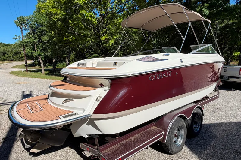 Slide: The Image of 2004 Cobalt 250 boat on trailer, featuring maroon and white design with canopy, parked outdoors. - 8