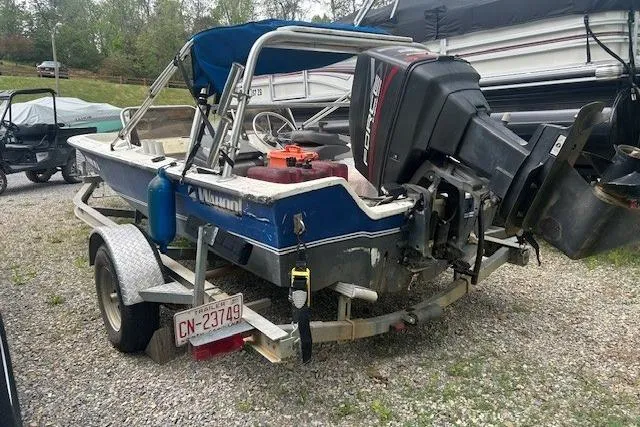 The Image of 1990 Wahoo 16.5 boat on trailer with outboard motor, parked on gravel. - 1