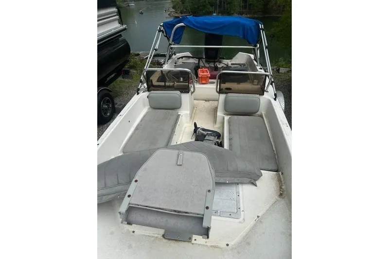 Slide: The Image of 1990 Wahoo 16.5 boat interior with gray seating and blue canopy, docked by a lake. - 3