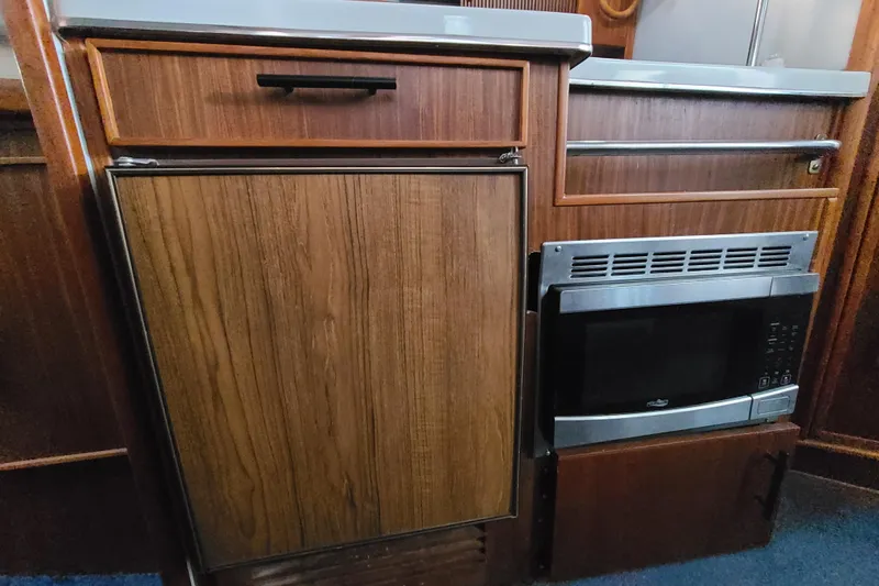 Slide: The Image of 1987 Sea Ray 300 Sundancer galley with wood cabinetry, microwave, and compact refrigerator. - 17