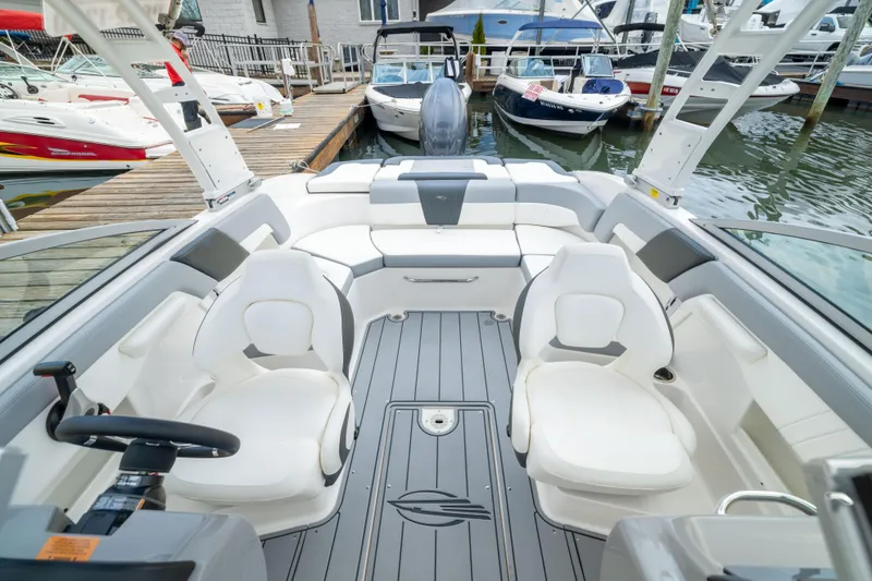 Slide: The Image of 2024 Chaparral 23 SSi OB boat interior with white seating and modern design at a marina. - 14