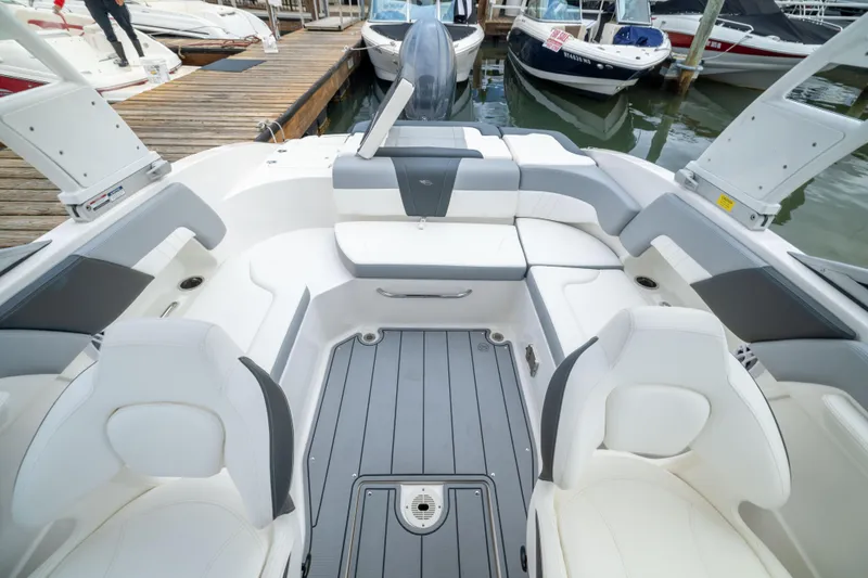 Slide: The Image of 2024 Chaparral 23 SSi OB boat interior with white seating and gray flooring at a marina. - 7