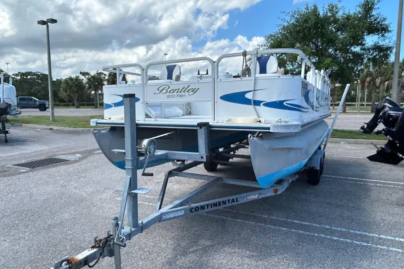 Slide: The Image of 2005 Bentley Pontoons 200 Fish on trailer in parking lot, under cloudy sky. - 3