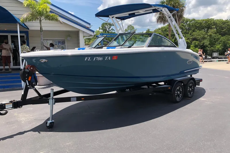 Slide: The Image of 2021 Cobalt CS22 boat on trailer, parked outside a building under a sunny sky. - 2