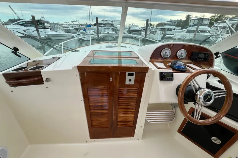 Slide: The Image of 2018 Hunt Yachts Harrier 25 helm with wooden accents, steering wheel, and marina view. - 19