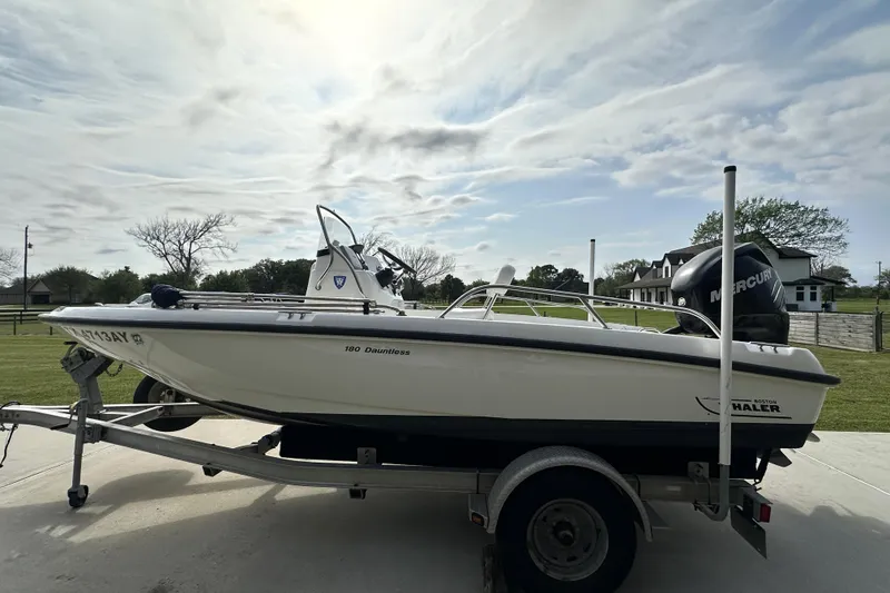 Slide: The Image of 2008 Boston Whaler 180 Dauntless boat on trailer, parked outdoors under cloudy sky. - 7