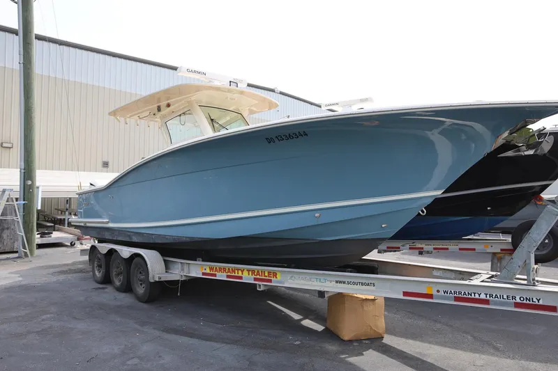 The Image of 2018 Scout 300 LXF boat on trailer, blue hull, parked outdoors. - 1