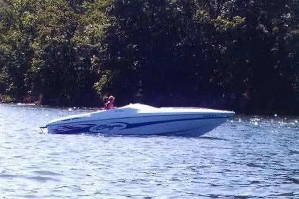 Slide: The Image of 1999 Baja 29 Outlaw speedboat cruising on a sunny lake with lush green trees. - 25