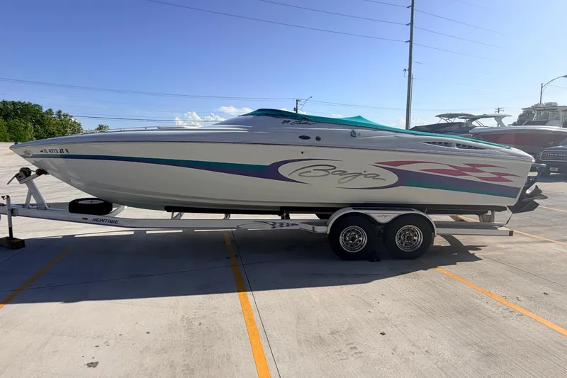 Slide: The Image of 1999 Baja 29 Outlaw speedboat on trailer, parked outdoors under clear sky. - 6