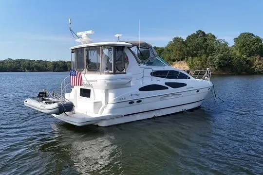 The Image of 2003 Cruisers Yachts 4050 Express on calm water, featuring sleek design and American flag. - 0