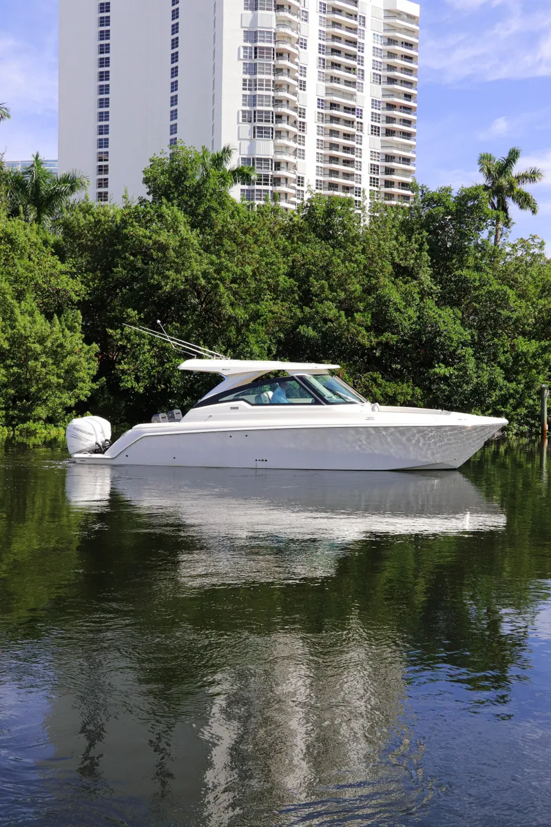 The Image of 2021 Tiara Sport 34 LX boat on calm water with trees and buildings in the background. - 0
