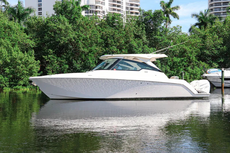 Slide: The Image of 2021 Tiara Sport 34 LX boat on calm water, surrounded by lush greenery. - 2