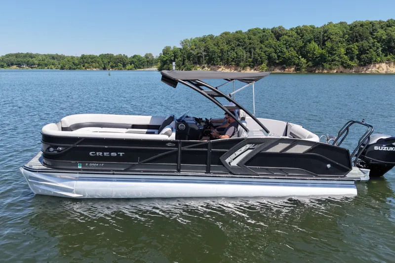 The Image of 2021 Crest RS250 pontoon boat on a serene lake with lush green shoreline. - 0
