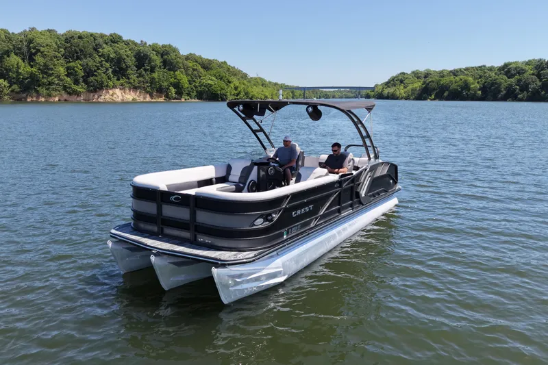 Slide: The Image of 2021 Crest RS250 pontoon boat cruising on a scenic lake with lush green shoreline. - 1